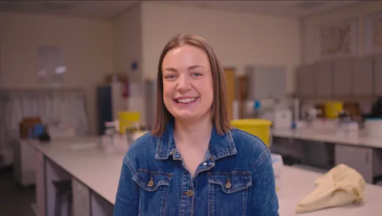 Medical Sciences student, Miriam, is smiling and looking off camera. She is sat in a science lab.