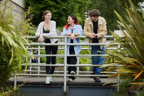 Three students laugh together while stood on a small bridge over a pond at Treforest campus