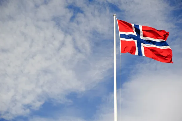 The flag of Norway flying in the wind with a blue sky in the background.