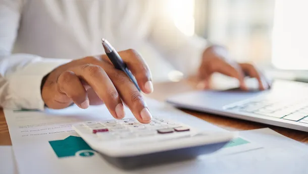 A close up of someone using a calculator and holding a pen whilst working out budgets.