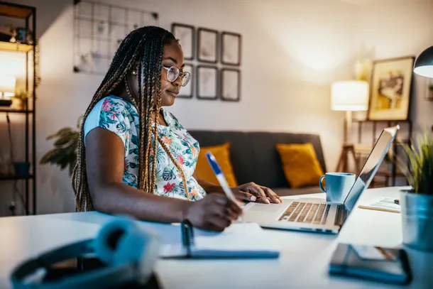 student studying from home at a laptop and taking notes
