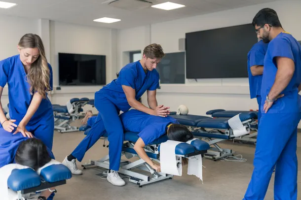 female and male student using chiropractic techniques on two other students, additional student is observing