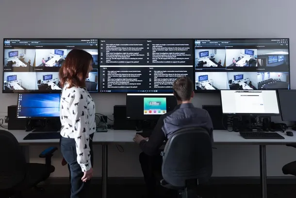 Two academics observing students on the screens in the hydra suite