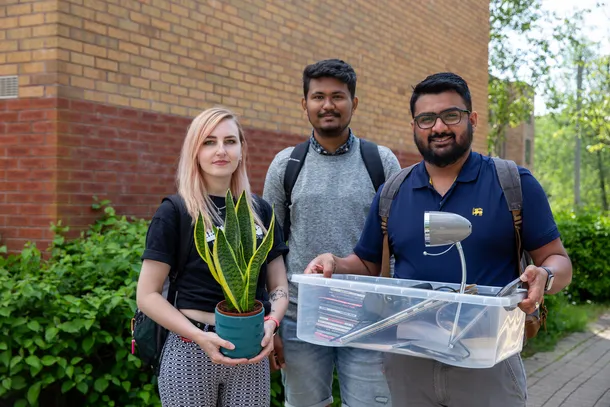 three students with moving boxes and a plant ready to move into student accommodation