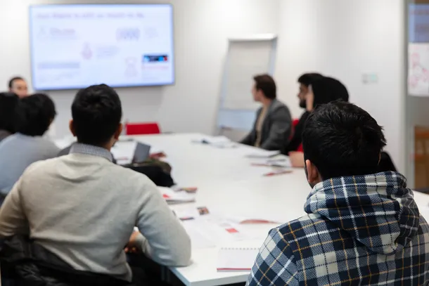students sitting around a table at business clinic watching presentation on screen