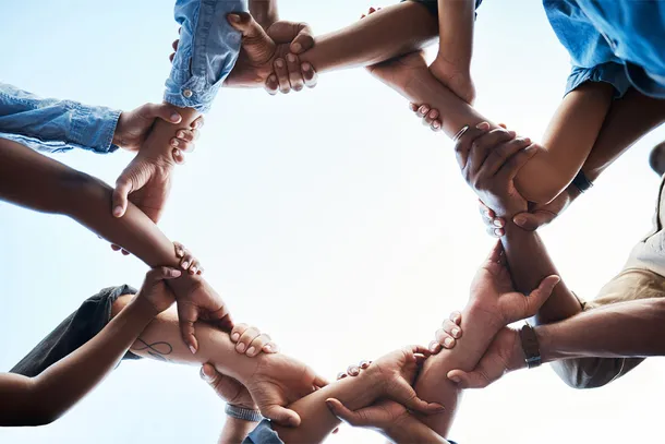 Low angle shot of an unrecognizable group of businesspeople standing together and holding each others arms in a circle