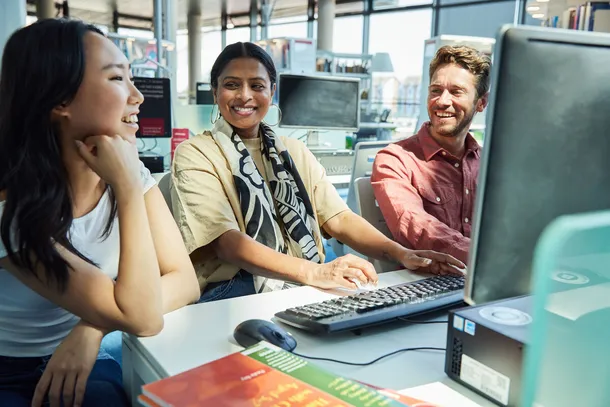 Three students sat together working at a desktop computer.