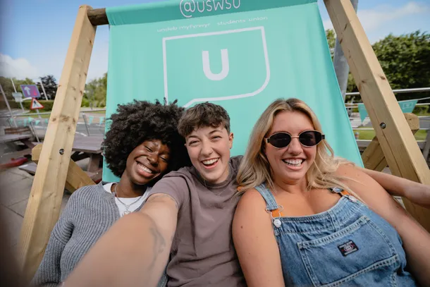 Three students taking a selfie on a giant blue deck chair.