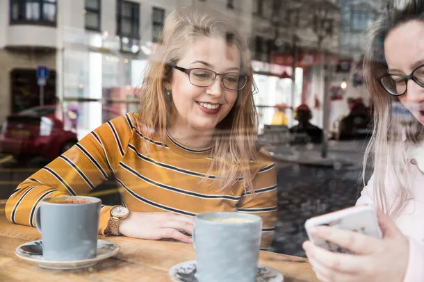 Students smiling and drinking coffee in a coffee shop.