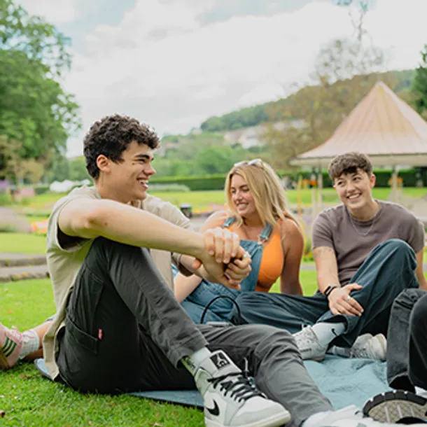 Students sat on the grass in a park, talking and smiling.