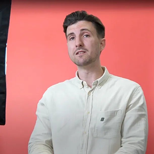 A member of USW staff talking to camera in front of a red backdrop.