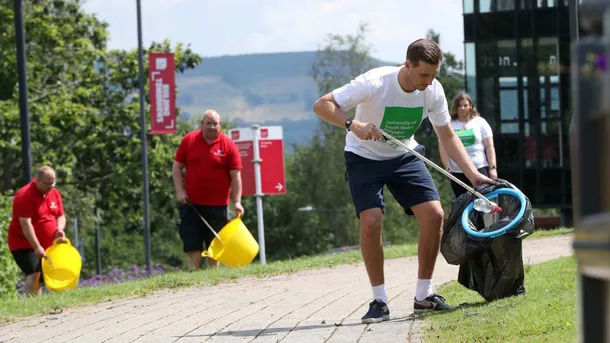 A male member of staff picking up litter on Treforest campus on a sunny day