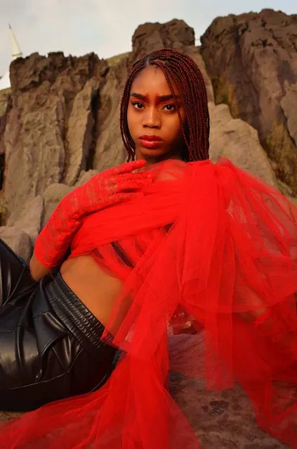 A black model poses dramatically in red clothes in front of sandy rocks