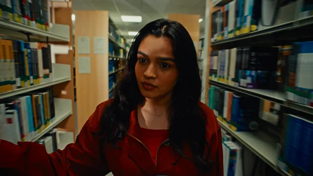 A law student in a red jacket browsing through tall bookshelves filled with books.