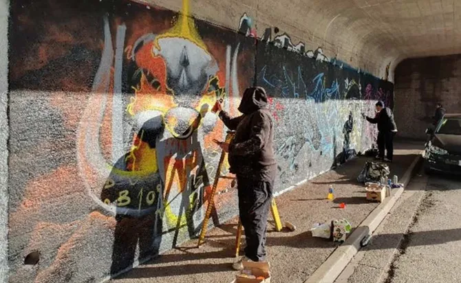 Two volunteers spraying artwork onto a wall.