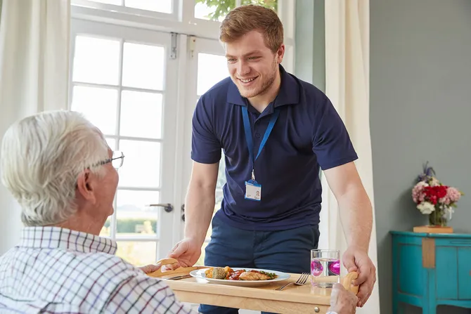 Male care worker serving food to a elderly man