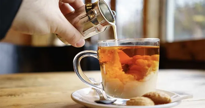 Milk being poured in to a small cup of tea