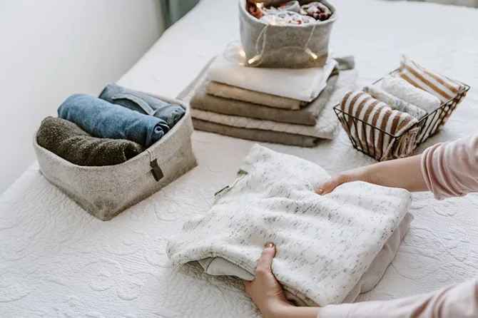 A person folding clothes in bedroom, organising laundry in boxes and baskets