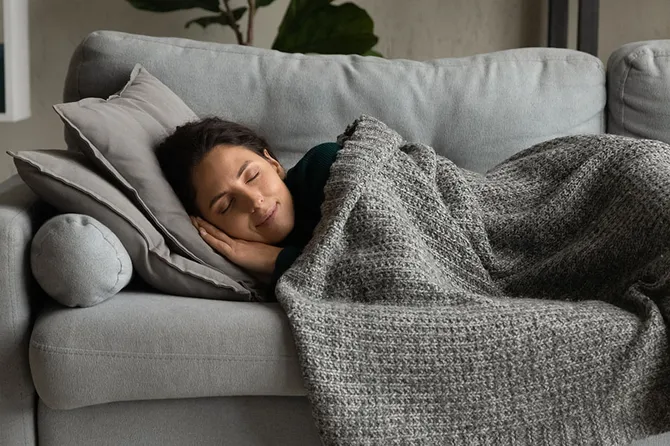 Young woman taking a nap on a sofa with a blanket