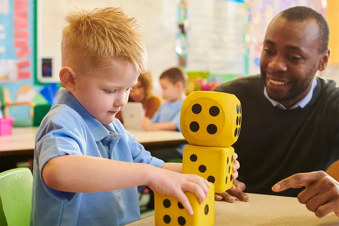 A teacher and young pupil play a numbers game using 3 foam dice