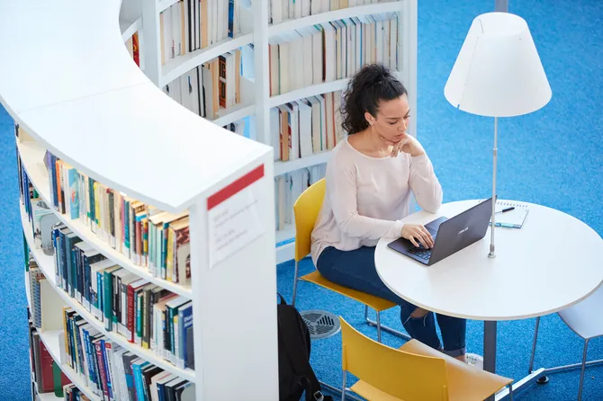 A student sitting at a desk in Newport library located between curved white bookcases.