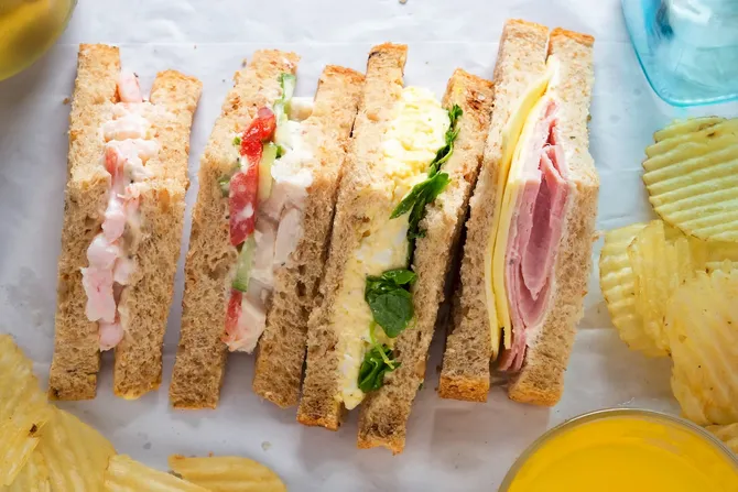 Selection of sandwiches on malted brown bread with crinkle cut crisps. Prawns with mayonnaise. Roast chicken breast, vine tomatoes, cucumber, mayonnaise. Egg mayonnaise and watercress. Ham and cheddar cheese on mayo.