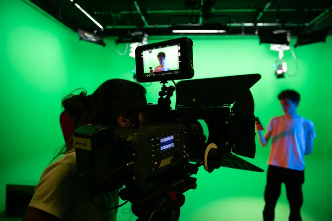 A student films another student in a green room with a large TV camera in the USW green screen studio