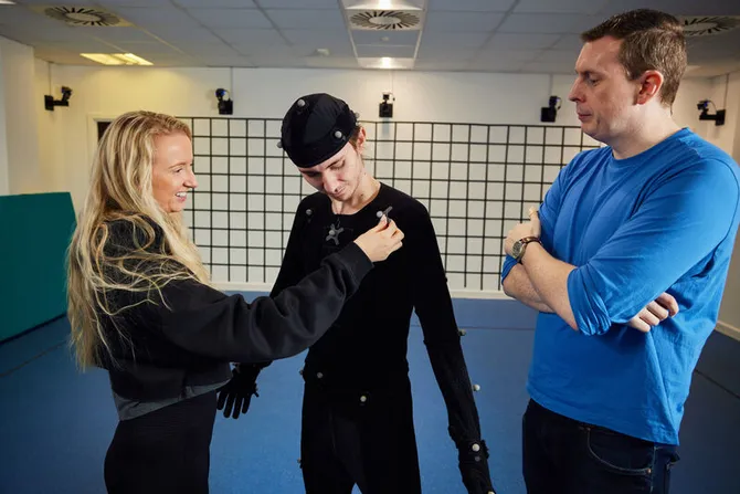 Two people assisting someone to dress in a motion capture suit.