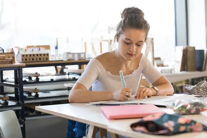 A student working in the interior design facilities with 3D models of buildings in the background.