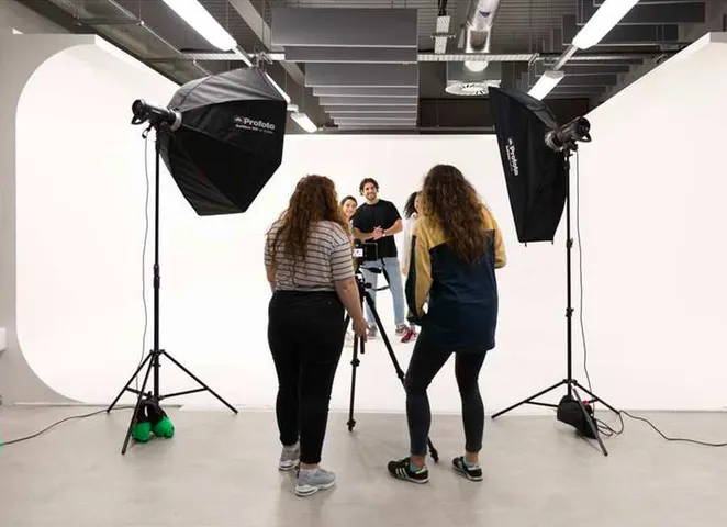 Students setting up professional lights and cameras to photograph two people stood against the white backdrop in the photography studio.