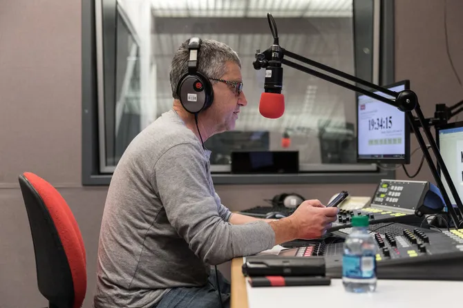 A person sat in the radio studio wearing headphones and talking into the radio microphone.