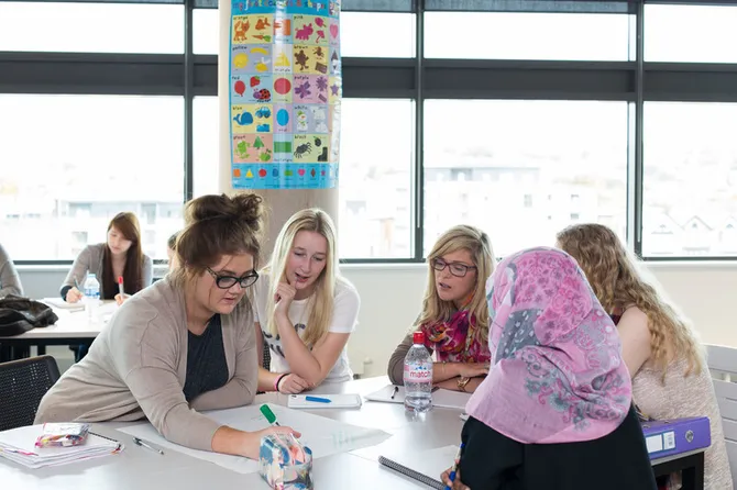 A group of students sat around a classroom table writing on a large sheet of paper.