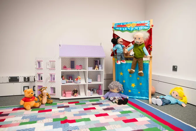A play therapy room filled with soft toys, a doll house and a puppet show stand.