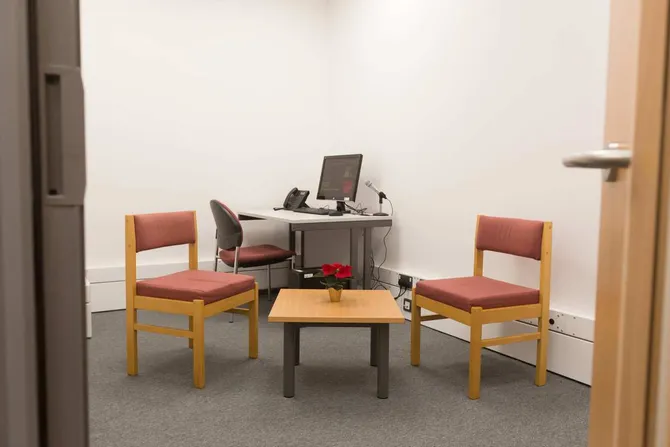 An empty therapy room. There is a desk with a computer, two chairs and a small table.