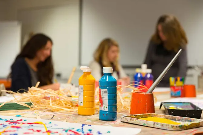 A close up of bottles of paint with students working on their artwork in the background.