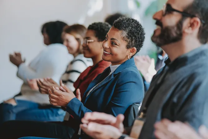 A group of people clap and listen intently in a conference room