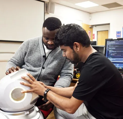 Two postgraduate artificial intelligence students work on a laptop in a USW Treforest computer laboratory with a computer in the background