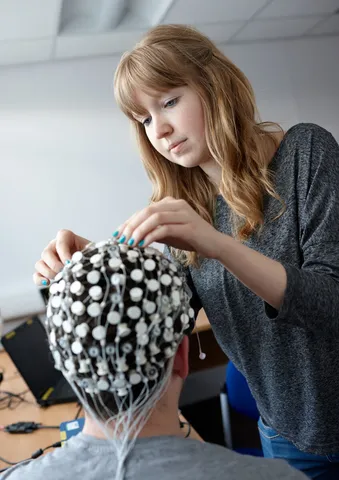 Psychology student fitting neuropsychology equipment on subject.