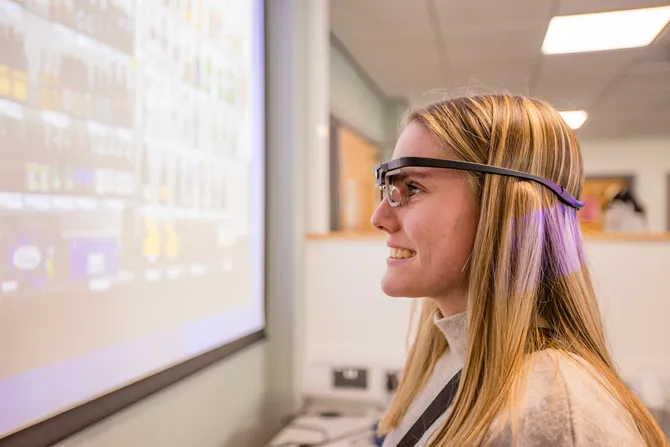 A student wears the eyetracker glasses while looking at a projection on a whiteboard as part of an experiment in a psychology laboratory in Glyntaff campus