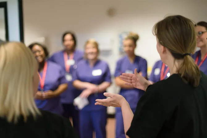 A group of nursing students stood in a line taking instructions from a nursing lecturer in the clinical simulation centre