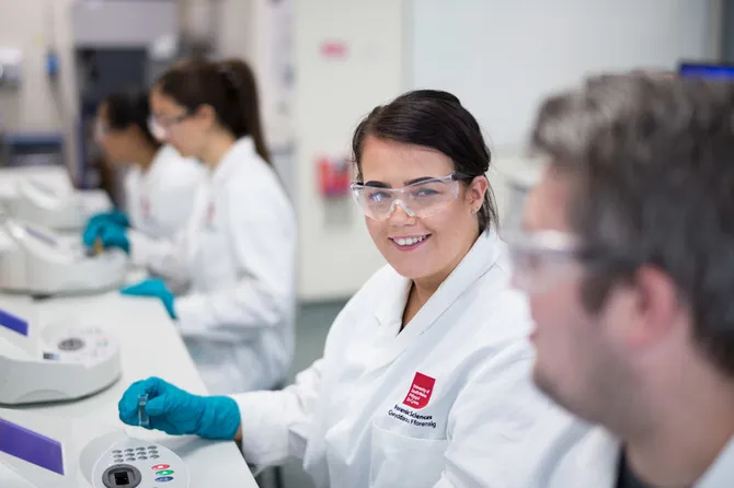 Students wearing lab coats and protective eyewear are working in a forensics lab.