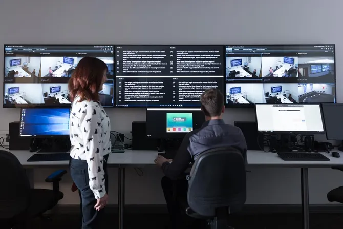 Two academics observing students on the screens in the hydra suite