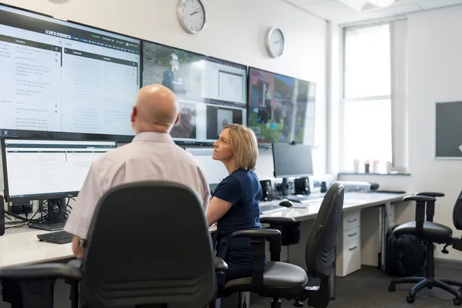Two people observing multiple TV and computer screens showing various evidence.