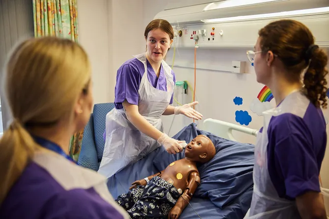 Three child nursing students examining a patient simulator.