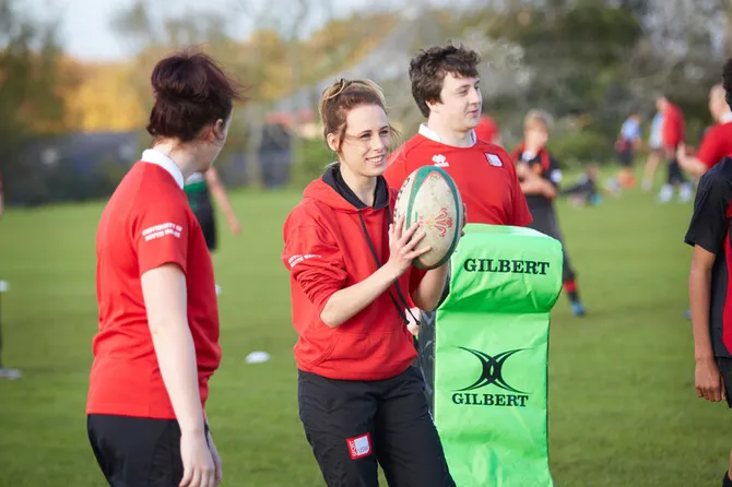 Two female students pitchside with rugby ball in hand.
