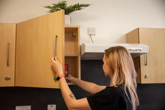 A student in mountail halls shared kitchen reaching into a kitchen cupboard pulling out a packet of rice to cook.