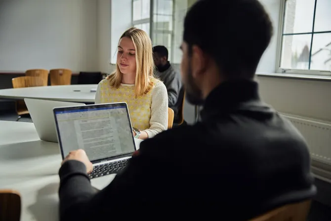 Two students sat at a table working on laptops