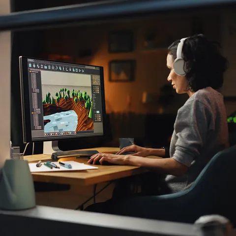 A person uses 3D animation software on a desktop PC to create a computer game world while sat at a desk