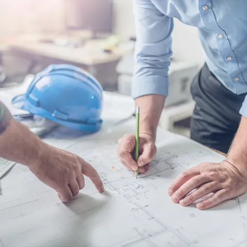 A close up of building plans being examined and annotated by two construction workers