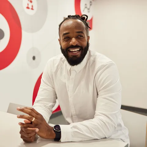 A lecturer laughs while sitting at a table in Treforest with a white and red wall in the background
